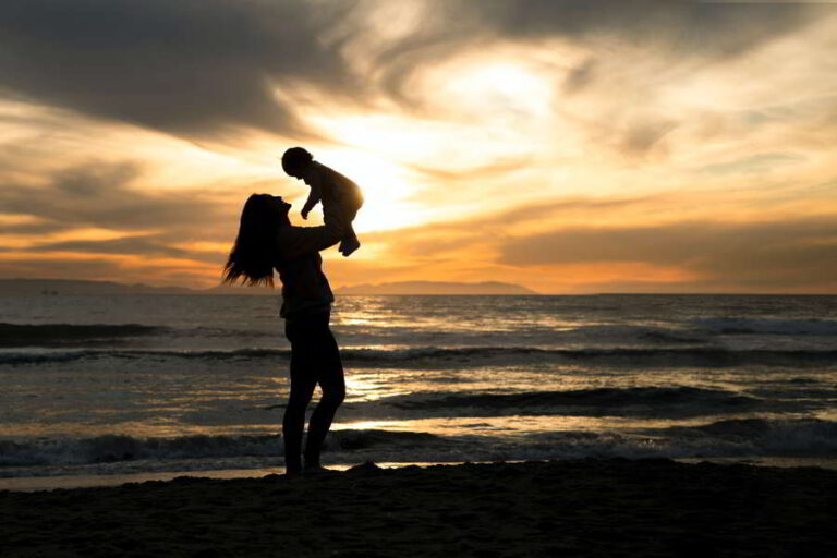Hyvää äitienpäivää äiti nostaa lasta rannalla auringonlaskussa